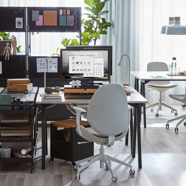 Compact home office setup with TROTTEN desk, monitor, supplies, plants, grey chair.