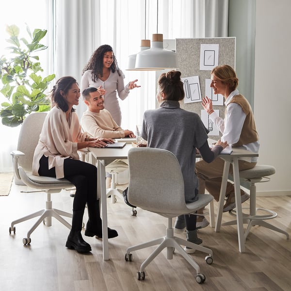 Five people collaborating at modern trottén desk, smiling while working on laptops, lemonade on table.