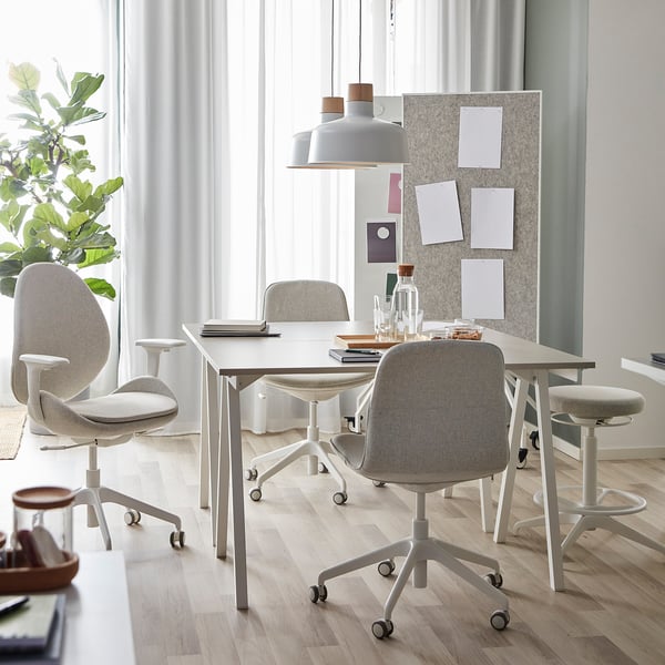 A modern home office a TROTTEN desk, grey chairs, and a pendant lamp. Spacious with a-legs and large windows, its bright and decorated with a plant.