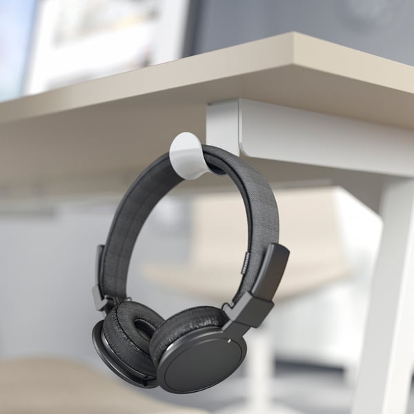 Black headphones hang on white hook under beige desk.