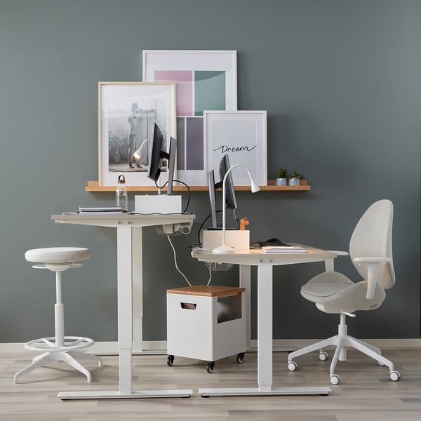 Home office setup with adjustable desk, stool, and computer monitor.