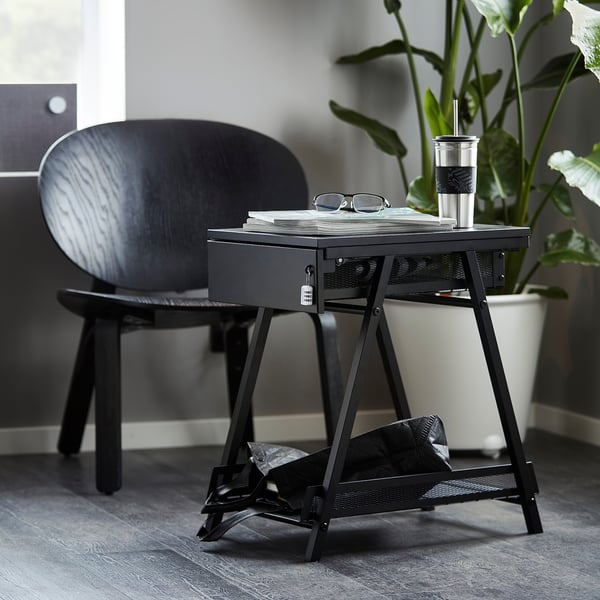 A black TROTTEN storage unit with drawer and shelf, beside a dark wooden chair. Lightweight, durable, space-efficient, ideal for a bicycle helmet.