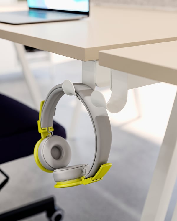 Grey and yellow headphones hang from a white hook under a white desk.