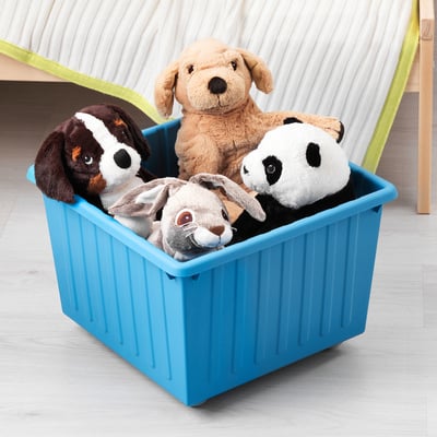 Blue storage basket holding stuffed animals. Four plush toys visible: two dogs, one cat, one panda. Basket has castor wheels for easy movement.