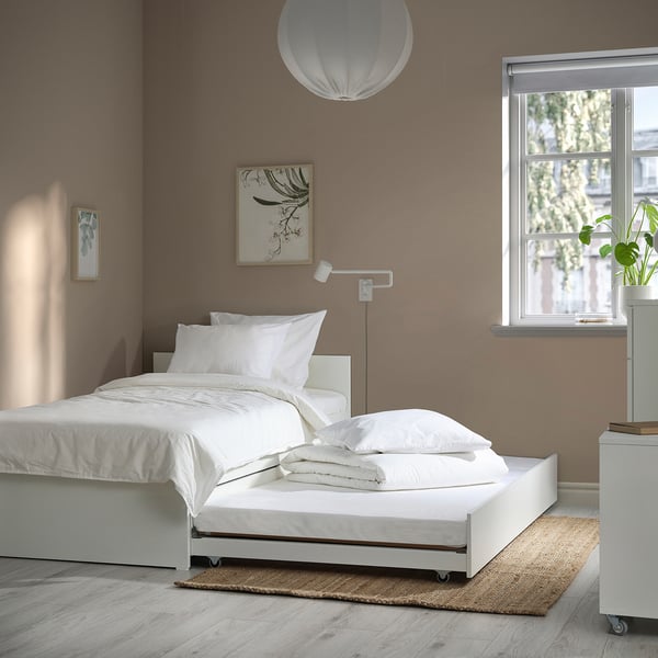 Modern bedroom with VIHALS white bed & trundle, clean linens, minimal decor, plant on small table.