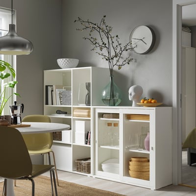 Modern living room with VIHALS storage series in white, glass cabinets, green chair, cosy rug, grey wall, mirror, and vase.