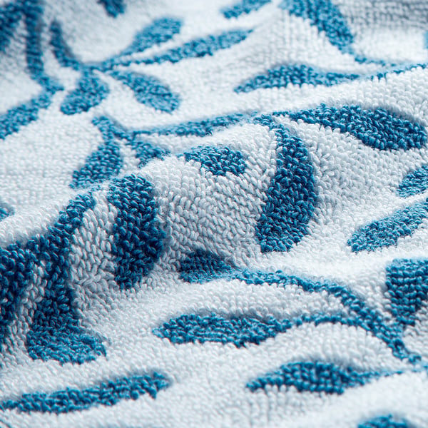 Close-up of soft, high-quality cotton towel with intricate blue leaf pattern. Texture shows elegant, absorbent weave.