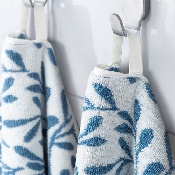 Two white towels with blue leaf patterns hang on hooks, one folded, displaying their decorative, absorbent design.