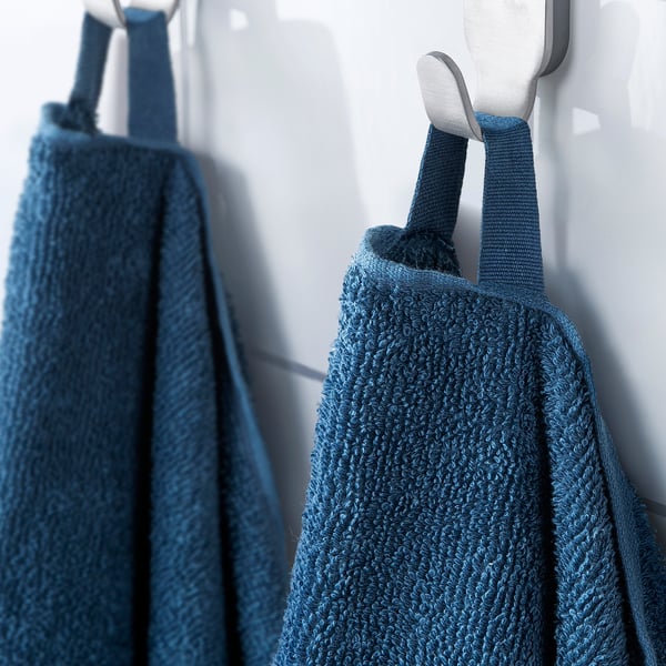 Two blue towels hang on silver hooks on a white wall. The towel on the left is folded, while the one on the right is draped over the hook.