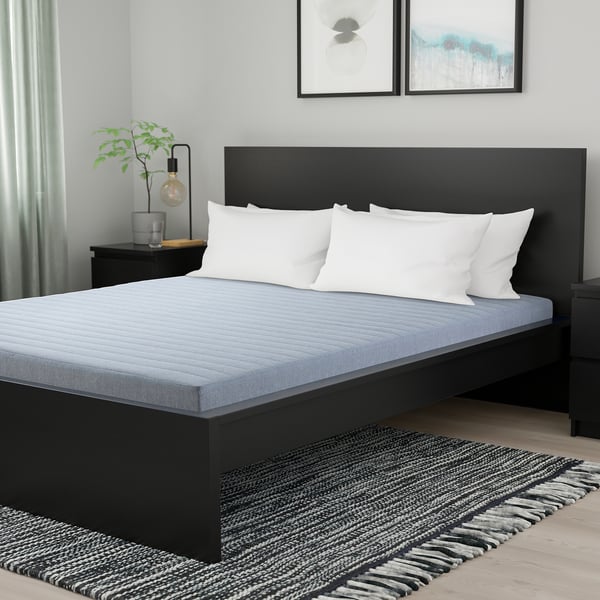 Black mattress with white pillows on dark bed frame, grey rug, plant & art.