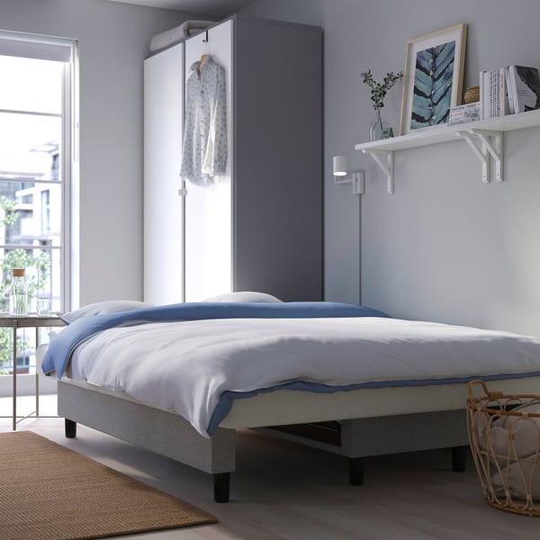 Modern sofa-bed in bedroom with storage, neatly arranged bedding, wall shelves, and city view.