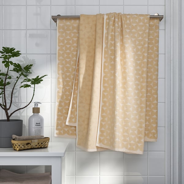 Yellow patterned towels hang neatly on metal bar near sink with soap dispenser and plant.