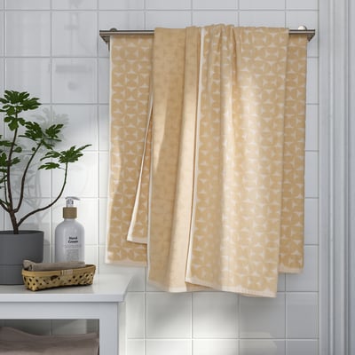 Yellow patterned towels hang neatly on metal bar near sink with soap dispenser and plant.