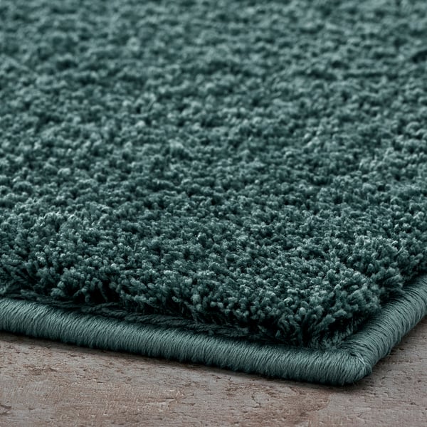 Thick, plush green bath mat with a soft, fluffy texture, likely made of recycled polyester, featuring a secure latex backing.