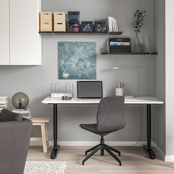 Modern home office: white BERGSHULT desk, grey chair, wall shelves with books & laptop.