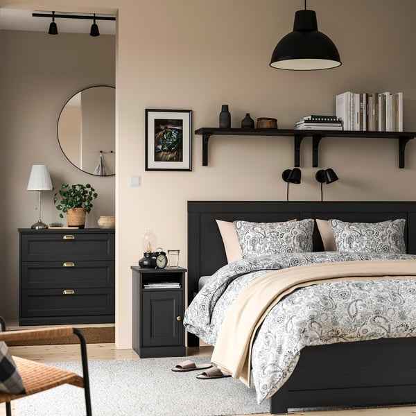 Modern bedroom with wall shelf, books, & decor. Patterned bedding, wooden floor, neutral walls, pendant light.