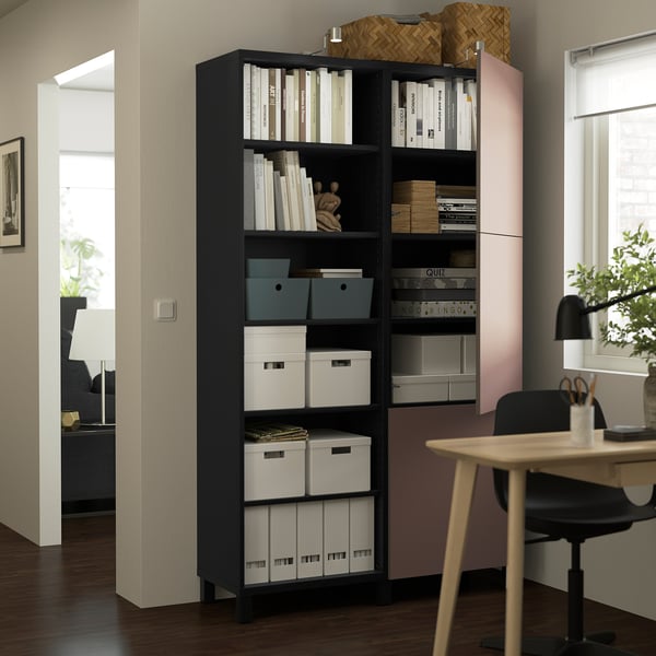 Black BESTÅ storage unit with shelves for books and storage boxes, next to a desk in a home office.