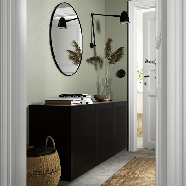 Modern hallway with black BESTÅ unit, mirror, and lamps. Floral arrangement, books, bowl, and basket.