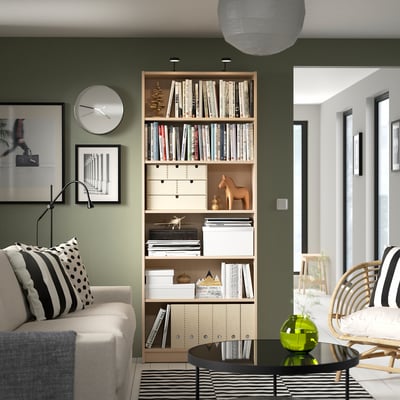 Stylish living room with BILLY bookcase between white sofa and wooden chair, holding books and decor.