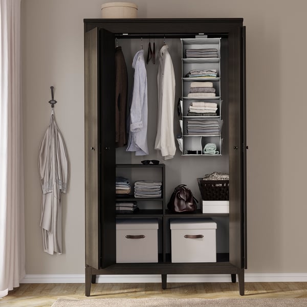 Dark wooden wardrobe with hangers, shelves, and fabric boxes. Clothes and accessories neatly organised.