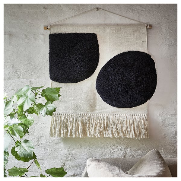 A BLANDSKOG wall hanging, featuring black geometric shapes, cream fringes, and a natural cotton material, creating a textured and minimalist design.