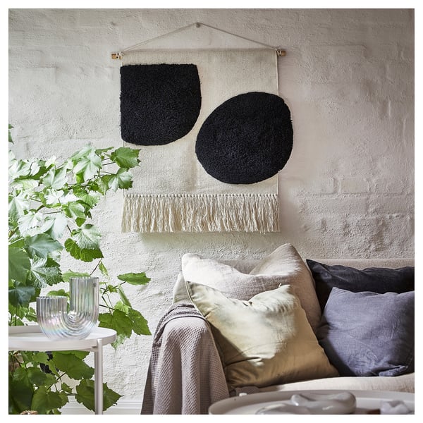 Cosy living room with a black and white geometric wall hanging, grey cushions, and green plant; modern decor.