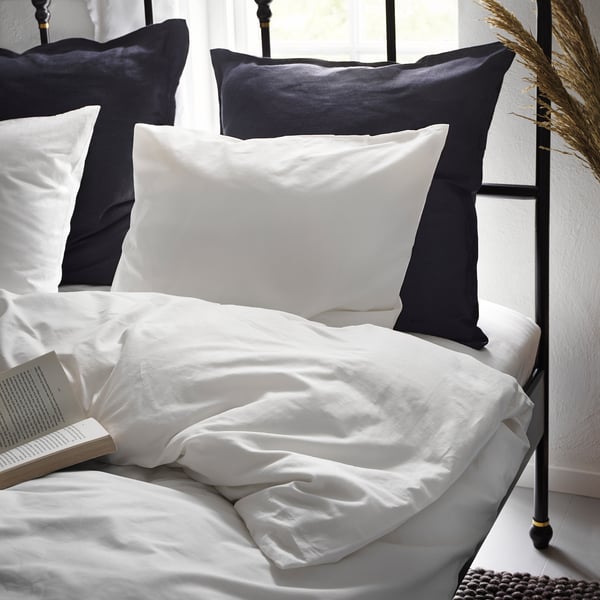 Cosy bed with white cotton duvet & pillows, black accents, open book, natural light.