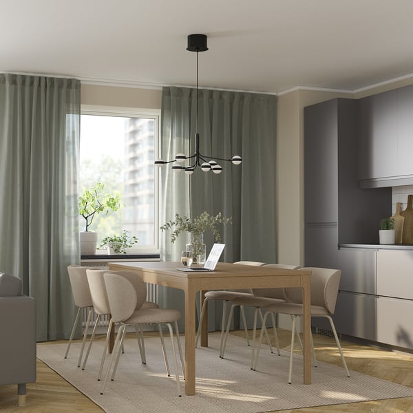 Modern dining area with EKEDALEN wooden table, beige chairs, black pendant light, green curtains, grey cabinet, cosy rug, and natural light.
