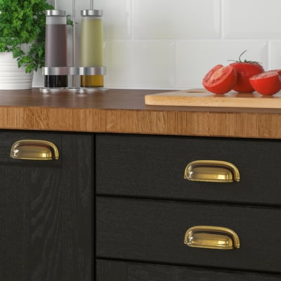 Black cabinets with gold handles and wooden countertop displaying sliced tomatoes, salt, pepper, and parsley.