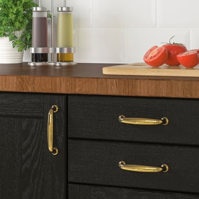 Black kitchen cabinets with brass handles displaying a cutting board and fresh tomatoes on a wooden countertop.
