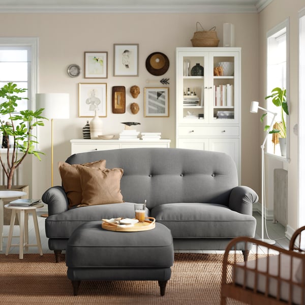 Modern living room: grey ESSEBODA sofa, brown pillows, wooden cabinet, plants, rug.