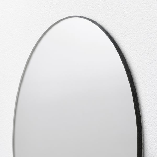 Oval mirror with sleek border, wall-mounted, reflecting light softly.