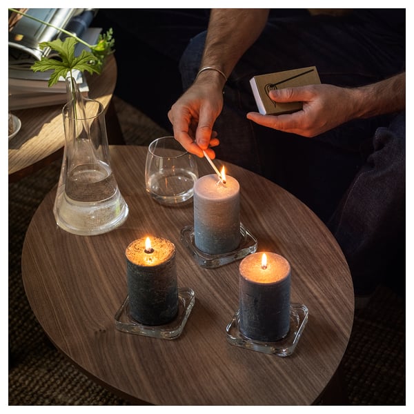 Person lights candle. Table has three candles, vase with plant.