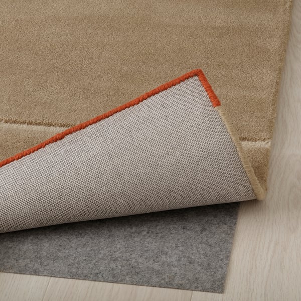 Rug with wool texture, red edge, folded back to show felted underlay. This setup prevents slippage and enhances comfort.