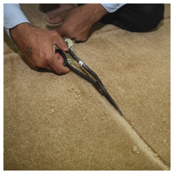 Person cuts beige GÅSHIRS wool rug with scissors. Handmade, natural, durable.