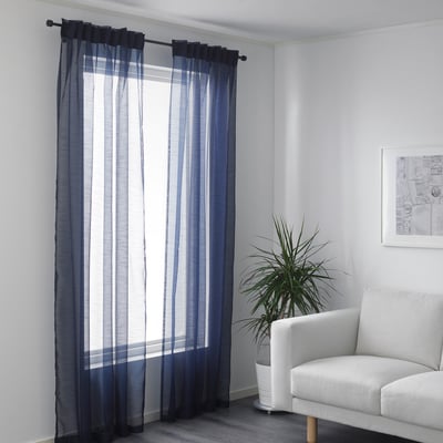 Living room corner with window, sheer blue-gray curtains, white armchair, and plant.