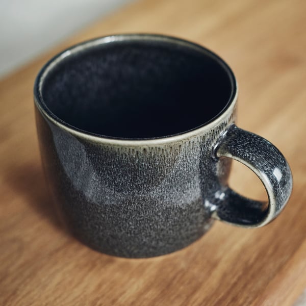 Dark grey glazed mug on wooden surface; smooth, handcrafted feel, part of the GLADELIG series.