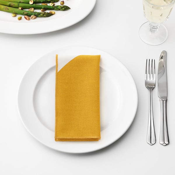 Table setting with yellow napkin, fork, knife, asparagus dish, and wine glass.