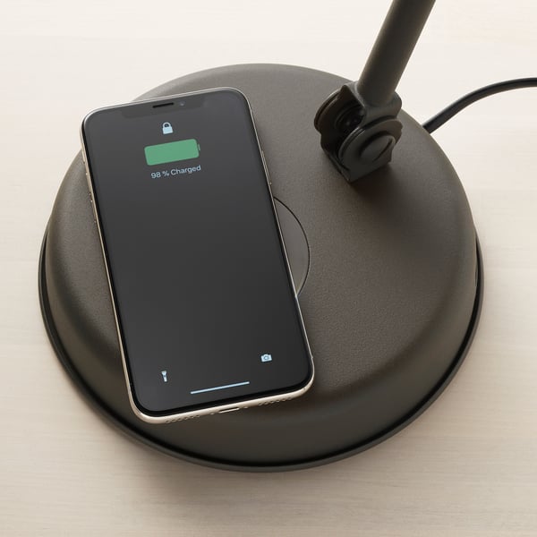 A smartphone displays 98% charged on a wireless charging pad integrated into a vintage-style lamp.