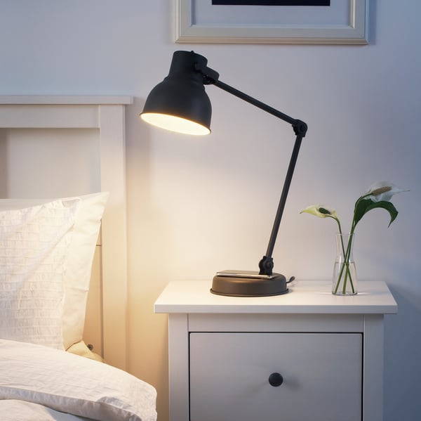 Modern HEKTAR lamp in black, adjusts to light book, rustic-contemporary design on bedside table with flowers.