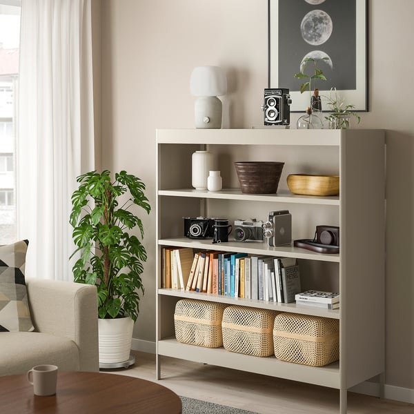 Beige IDÅSEN steel bookshelf with books, cameras, plant.