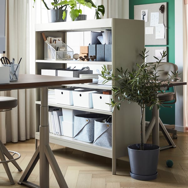 Modern office space with IDÅSEN grey shelving. It holds plants, books, and supplies. A desk with chair is nearby.