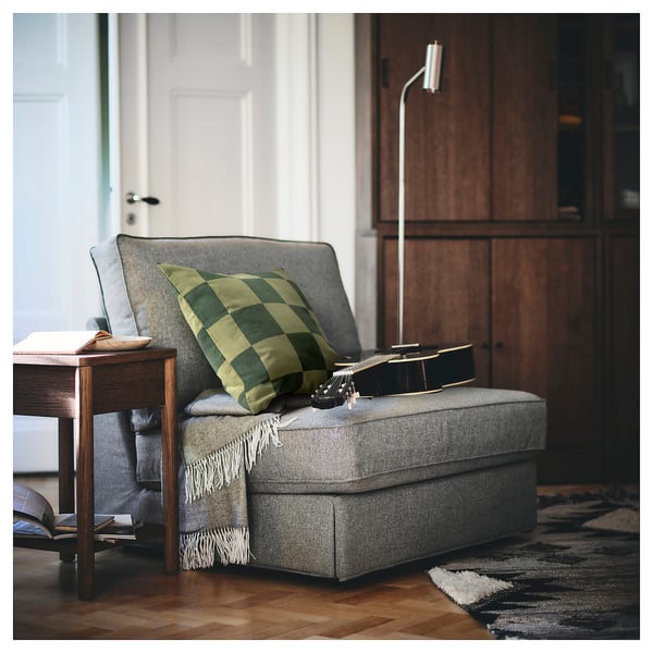 Cosy reading nook with modern armchair, green chequered pillow, guitar, and wooden table.