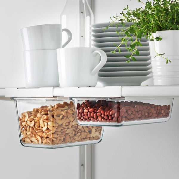 Under-shelf storage holders with cashews and beans containers, mugs, plates, and herb plant.