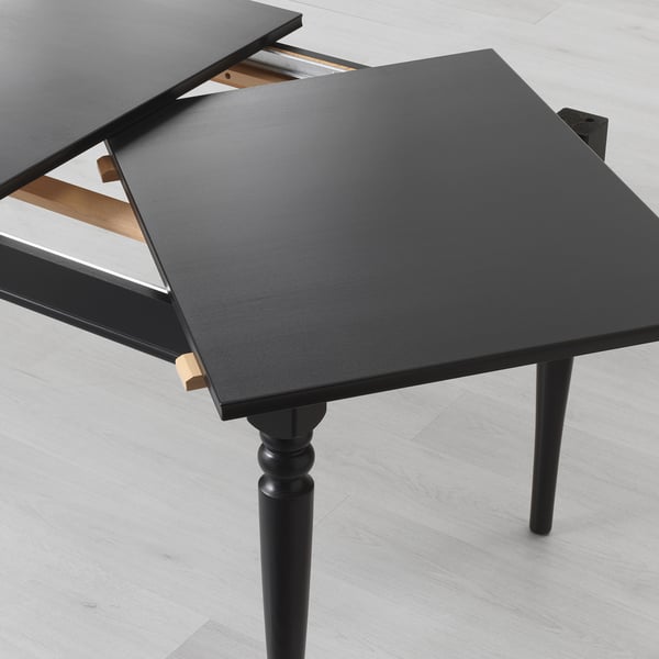 Black extendable dining table with one leaf added, standing on dark wooden legs.
