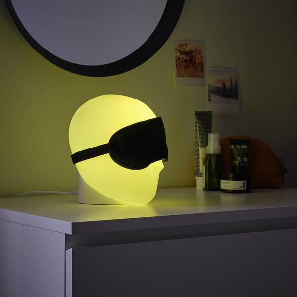 ISKÄRNA lamp in yellow, plastic, round with sleep mask, on table with items.