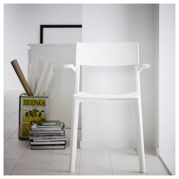 A white JANINGE plastic chair with a clean design, ready-assembled and stackable, next to a book and magazine holder with items inside.