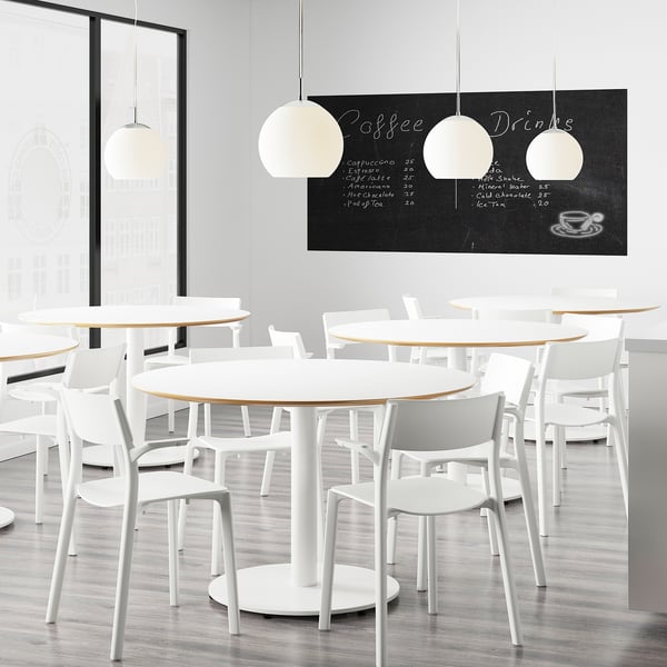 Modern café with white tables and chairs, large pendant lights, and a chalkboard menu listing coffee and drinks.