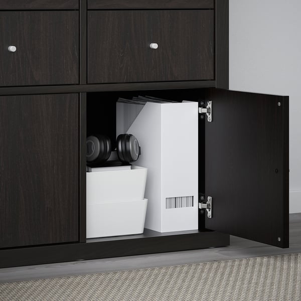 Black KALLAX shelf with door open, showing organised storage including white boxes and black headphones.