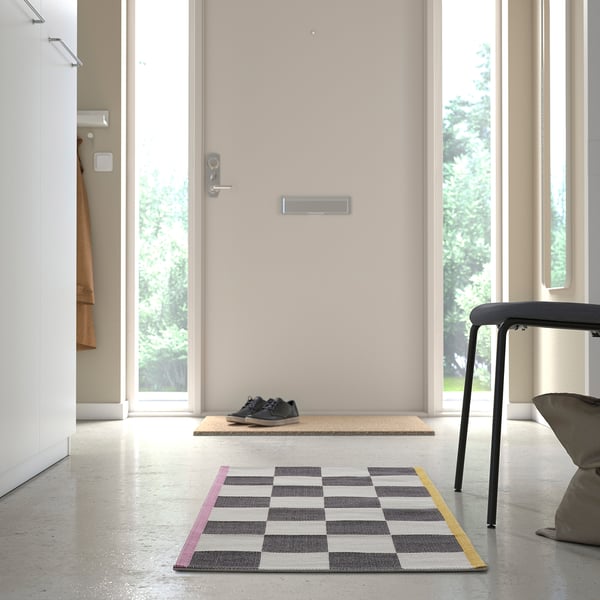 KLASSRUM rug in grey and yellow, square-shaped with checkerboard pattern, fits well under a stool, adding a retro vibe to the entryway.